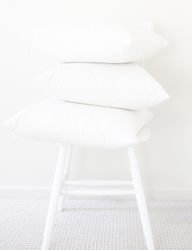 A stack of white pillow inserts on a white chair.