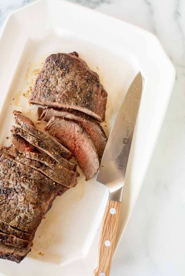 A perfectly cooked steak rests on a pristine white plate, ready to be sliced delicately with a glistening knife.