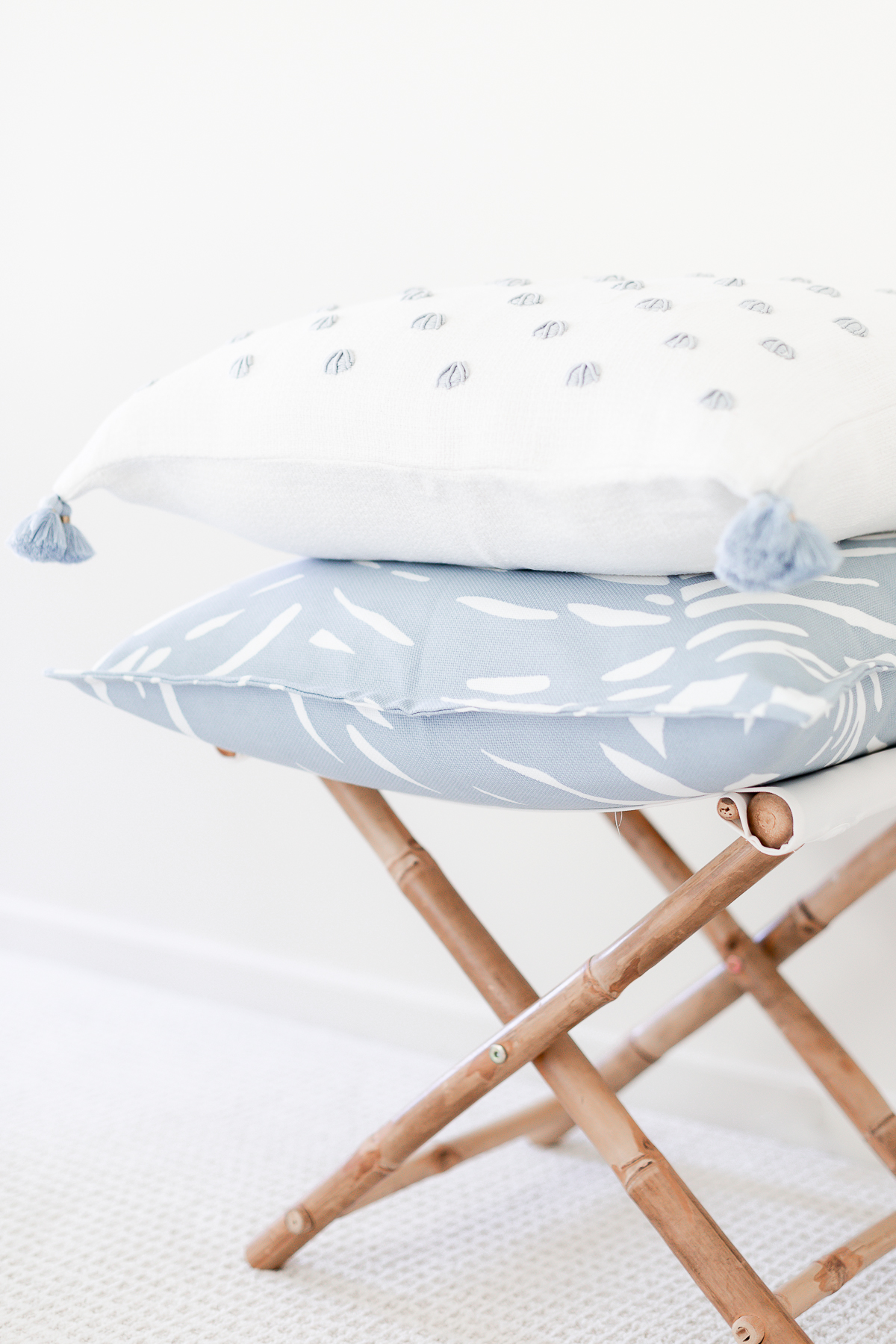 Two blue and white pillows with pillow inserts, stacked on a rattan stool.