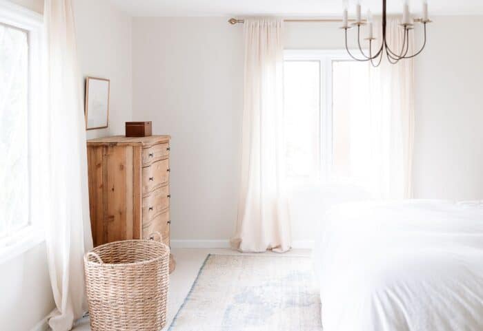 A white bedroom with a wooden dresser and the right size rug for a king bed.