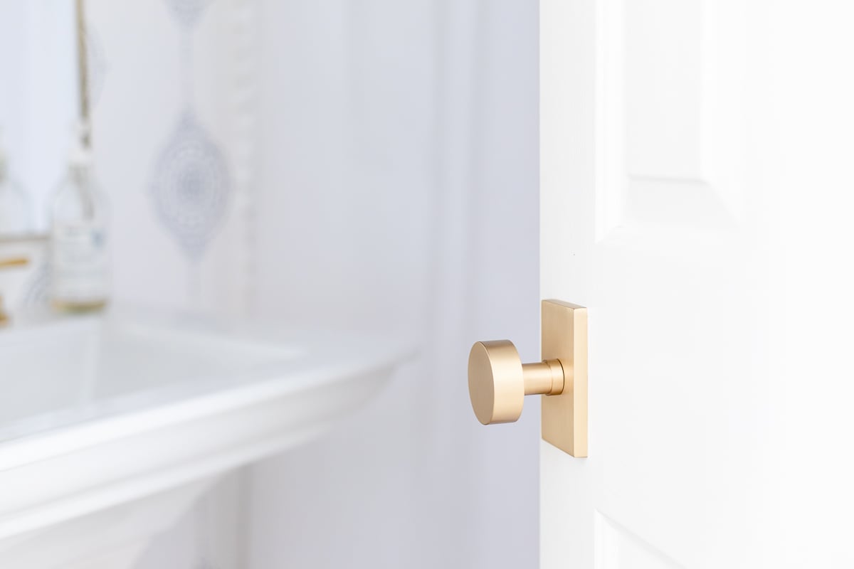 A modern door knob on a white door leading in to a wallpapered bathroom.