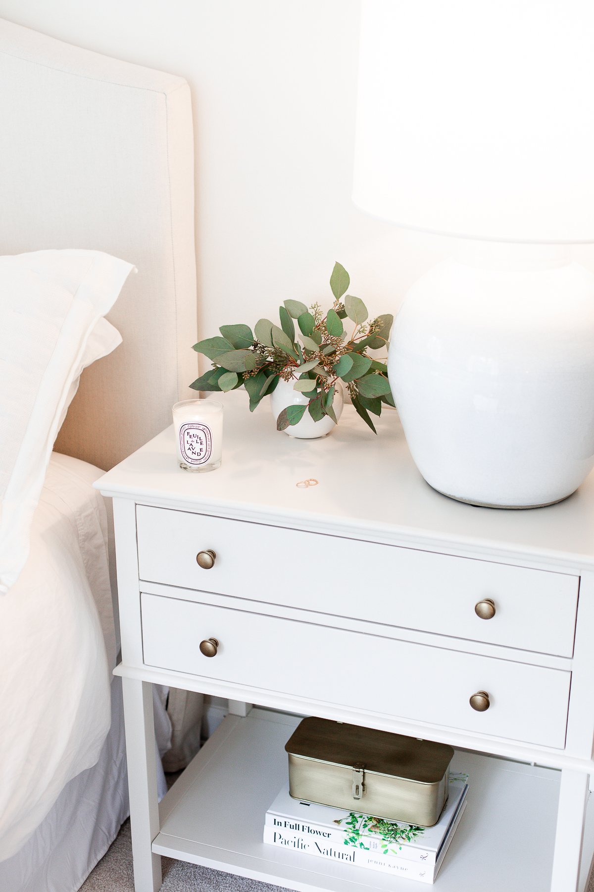 nightstand with lamp, a vase of greenery and candle