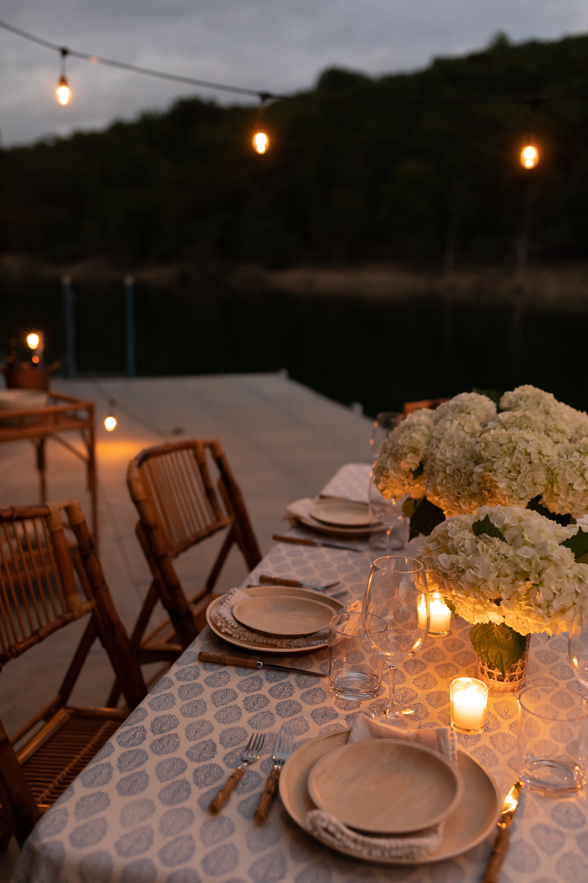 A blue and white table cloth set with bamboo plates and an al fresco dining view of the water