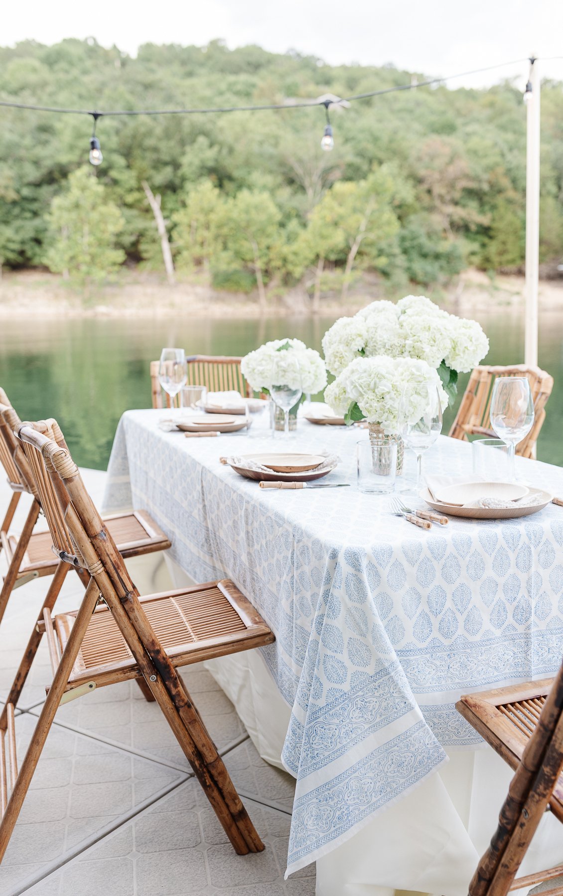 A blue and white table cloth set with bamboo plates and an al fresco dining view.