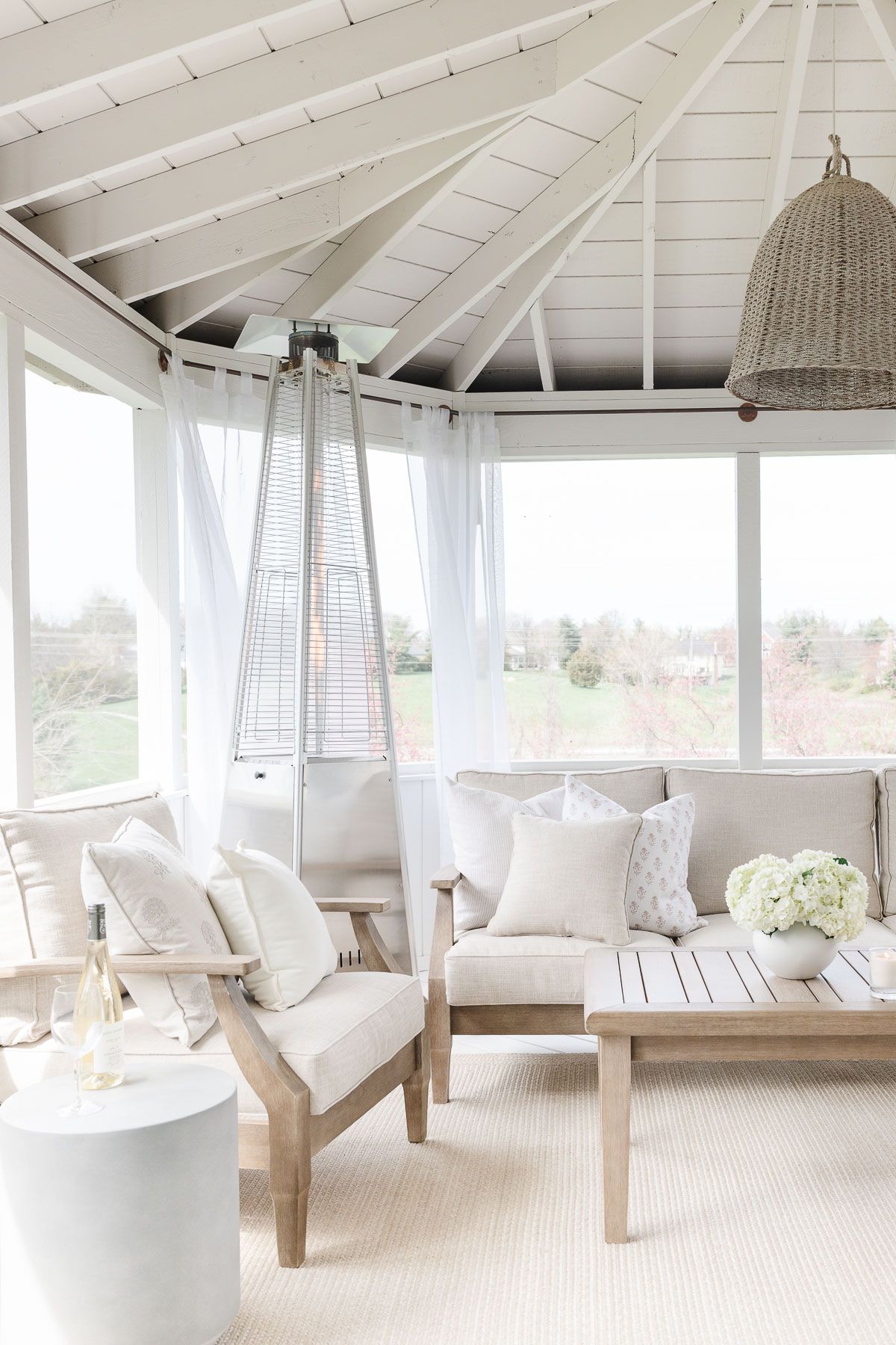 A screened in porch with light wood furniture. 