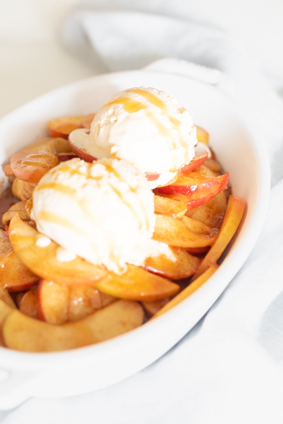 A white dish filled with baked apple slices and ice cream.