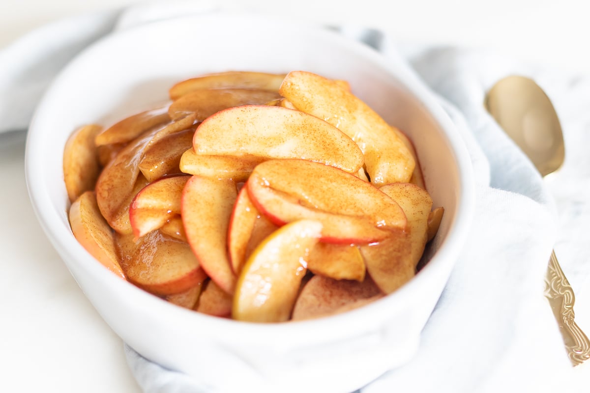 Baked apple slices presented in a white bowl with a spoon.