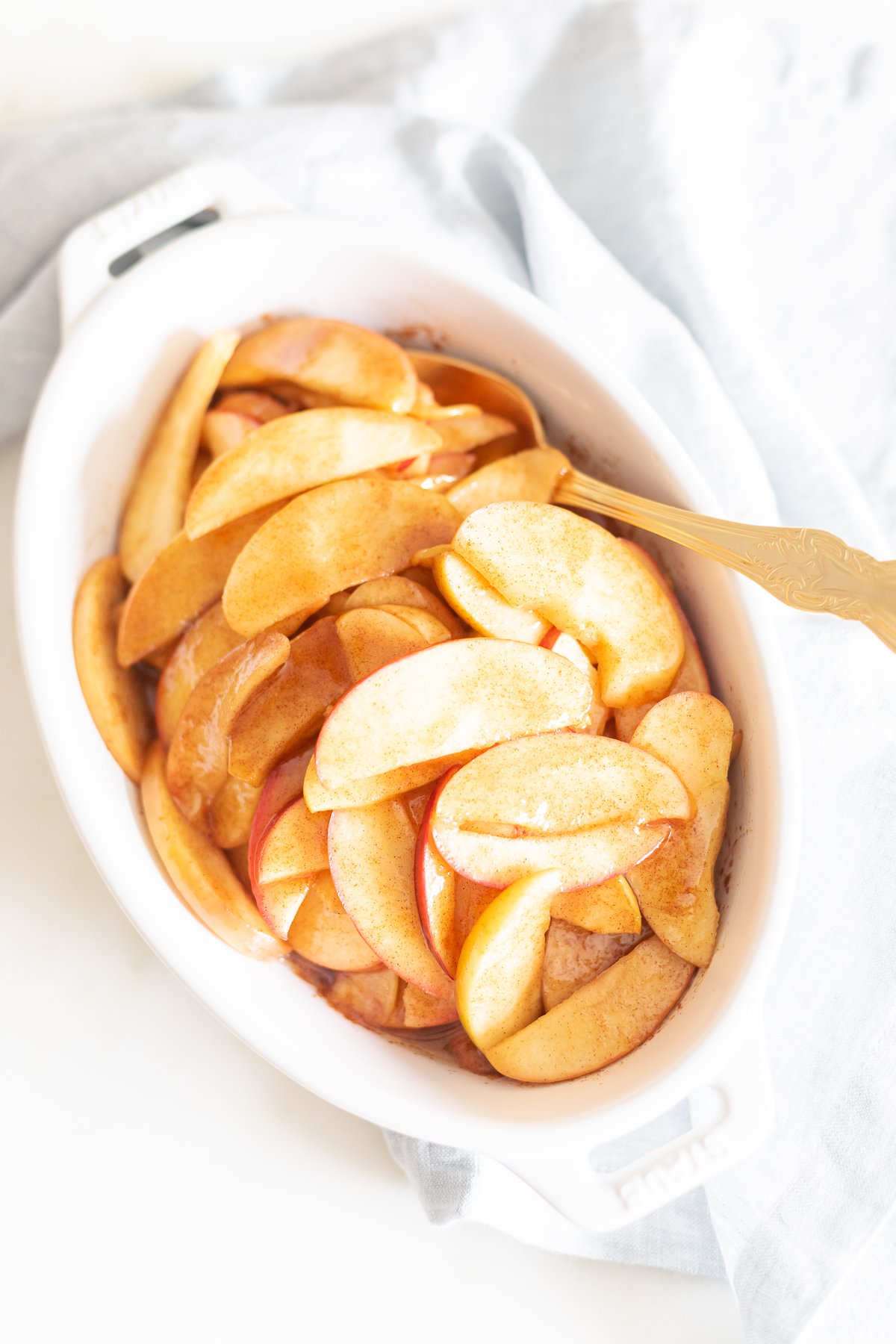 Baked apple slices in a white bowl with a spoon.