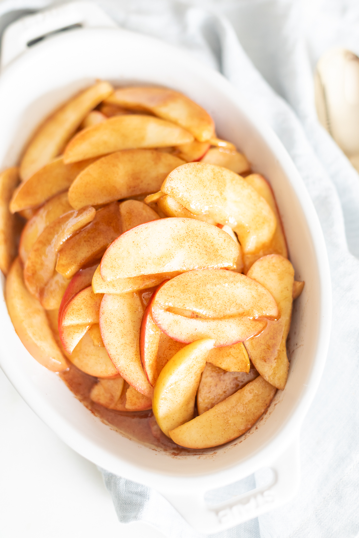 Baked apple slices arranged in a white dish with a spoon.