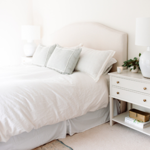 A white bed with pillows and a white nightstand in a bedroom.