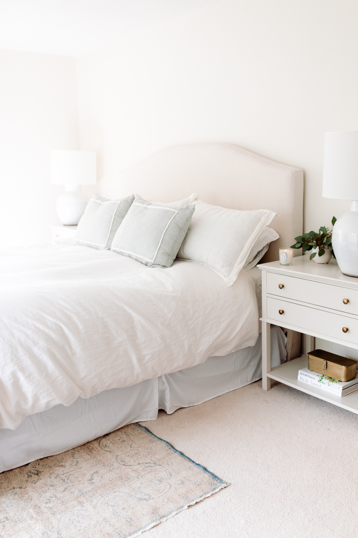 A white bed with pillows and a white nightstand in a bedroom.