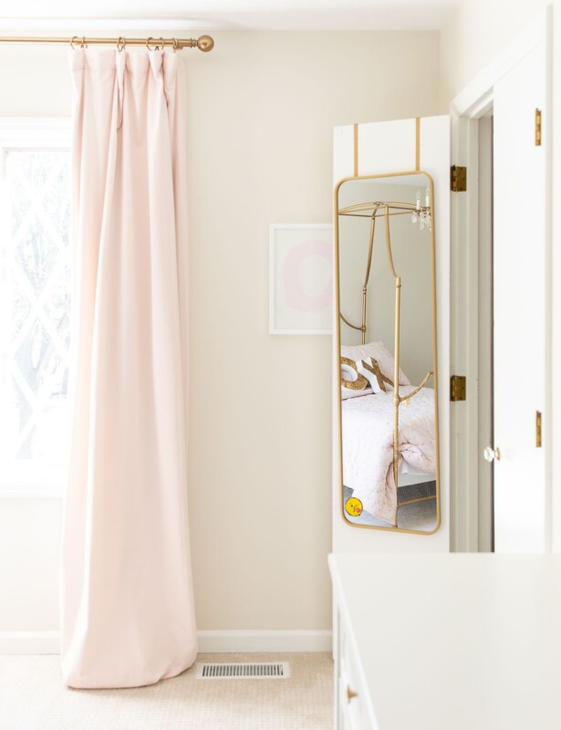 A girl's bedroom with pink blackout curtains and a mirror hanging on a closet door.