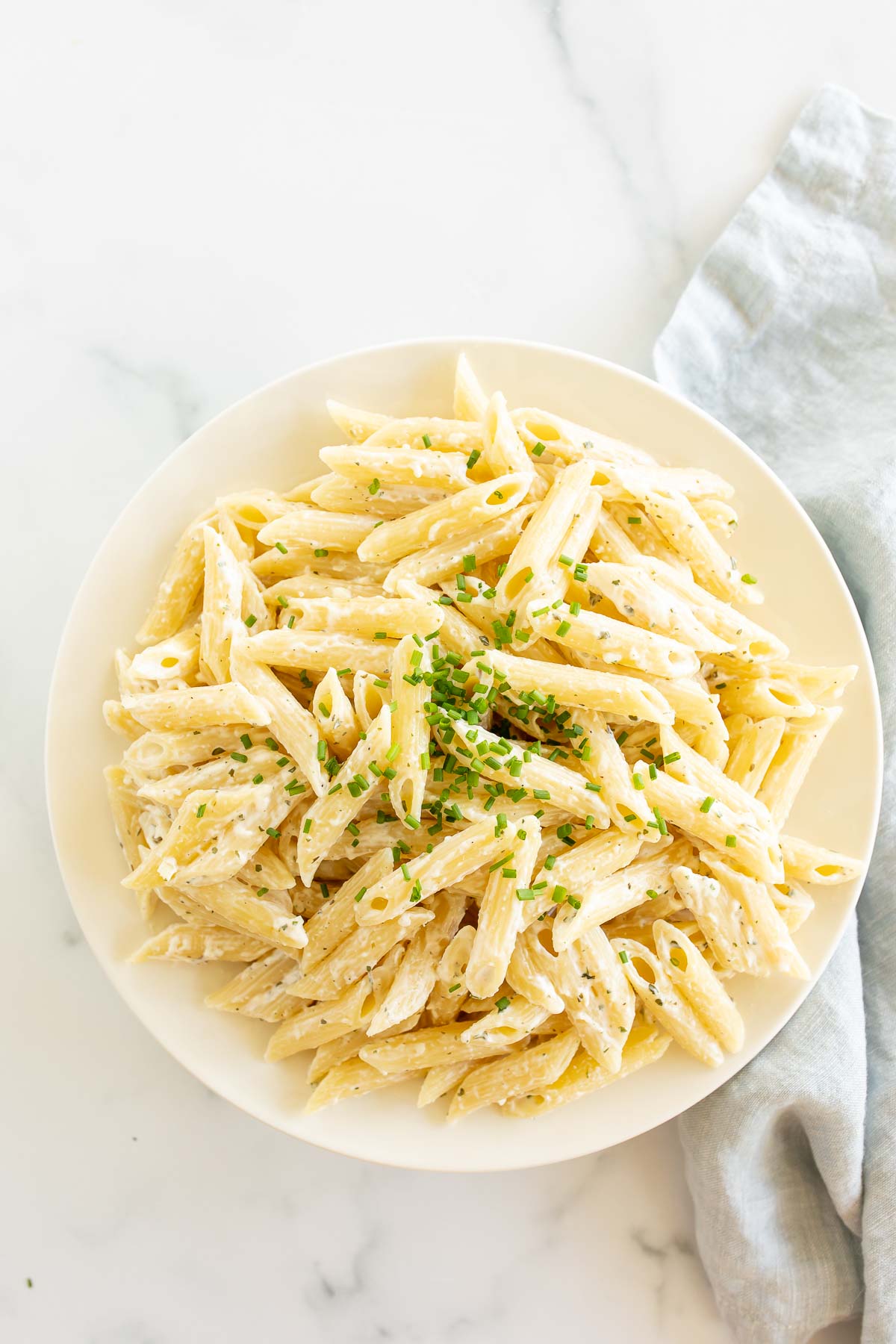 A white serving bowl full of Boursin pasta topped with chives.