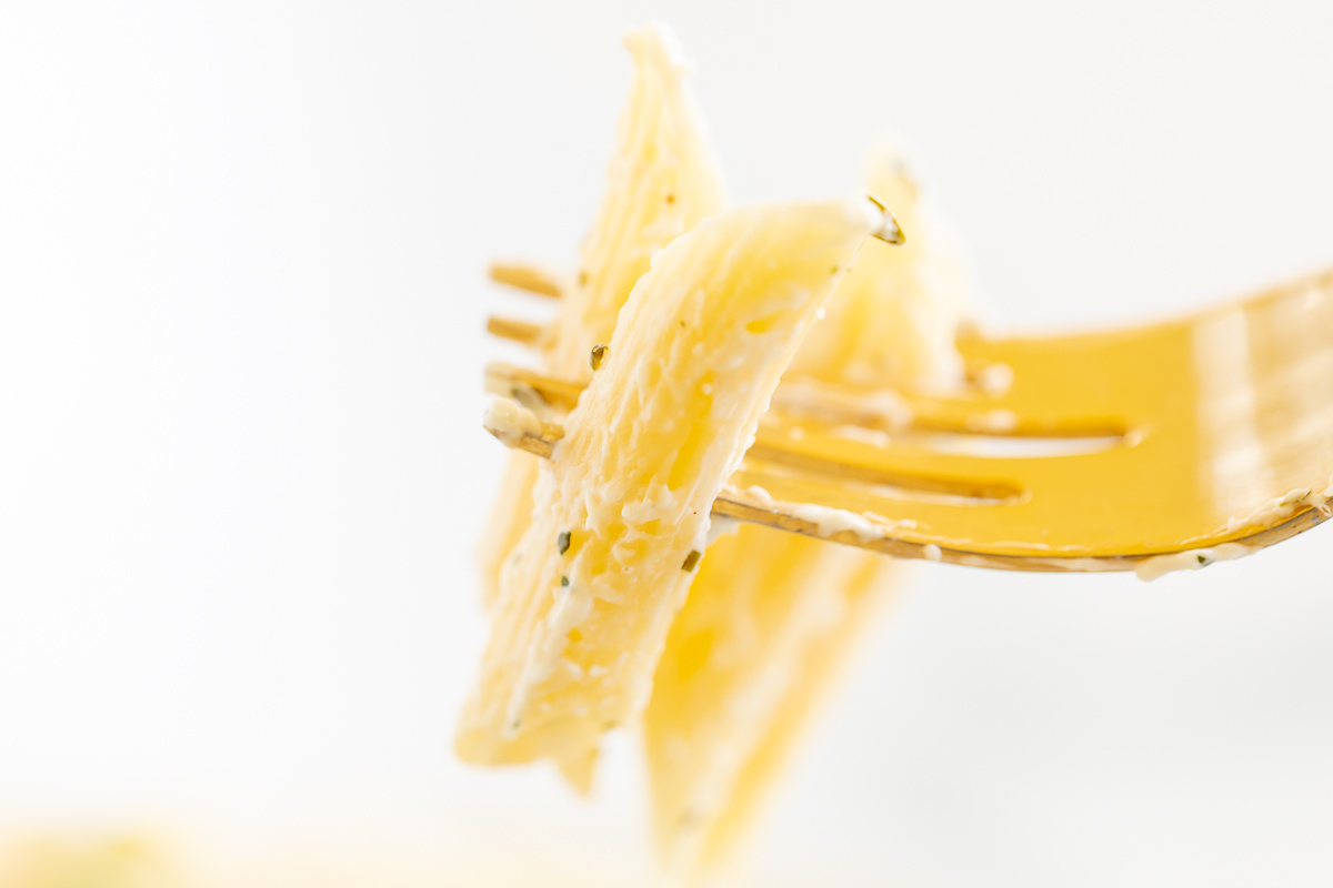 A fork holding a bite of boursin pasta against a white background
