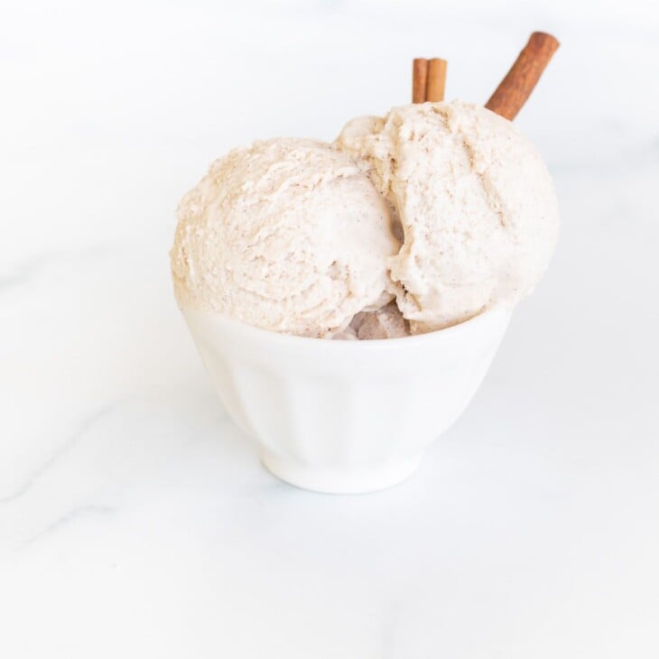 A white bowl full of homemade cinnamon ice cream with a cinnamon stick as garnish on the side