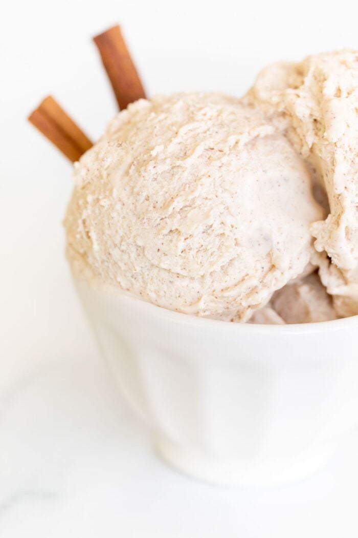 A white bowl full of homemade cinnamon ice cream with a cinnamon stick as garnish on the side