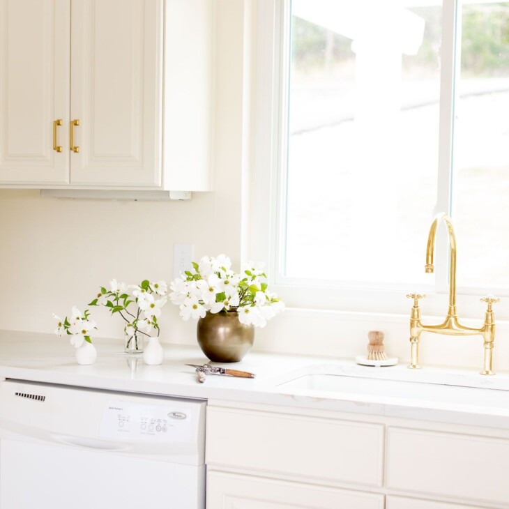 A white quartz countertop with an eased countertop edge, brass faucet on the sink in a cream kitchen.