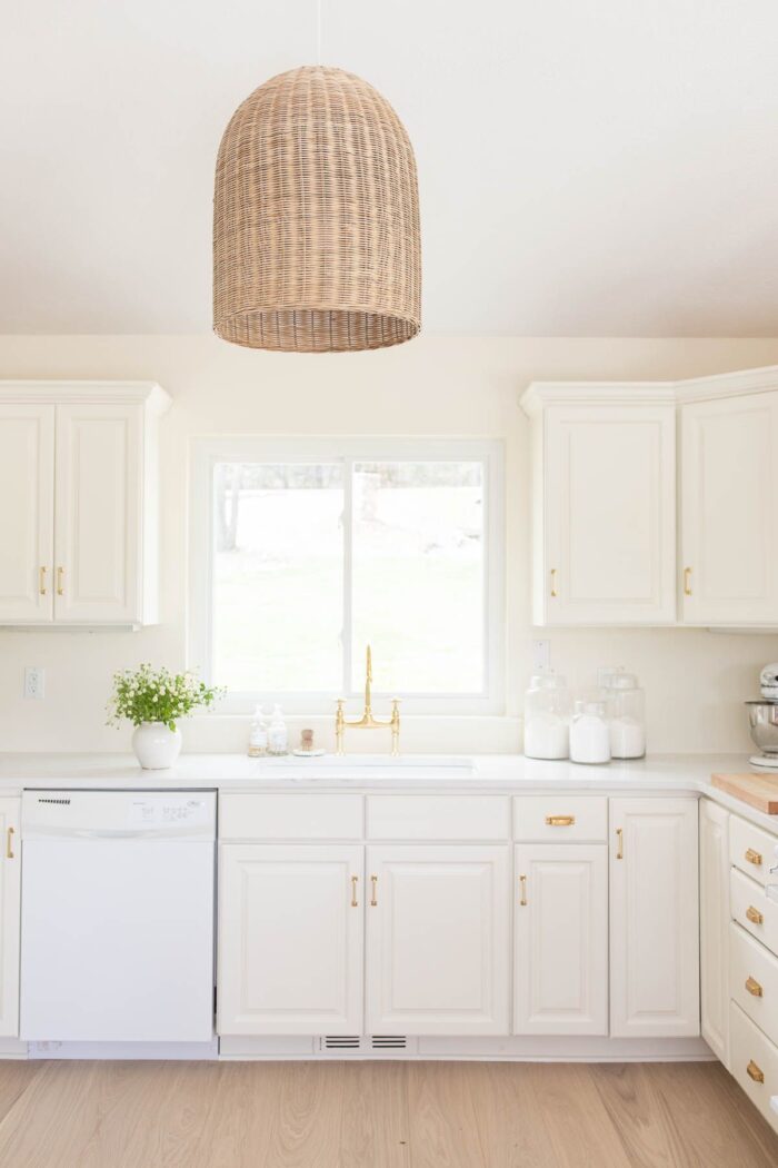 A cream painted kitchen with a basket light fixture and quartz countertops.