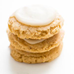 A stack of frosted pumpkin sugar cookies on a white surface
