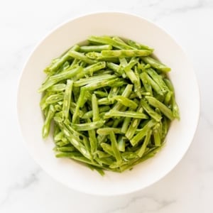 A white bowl on a marble surface, filled with French green beans.
