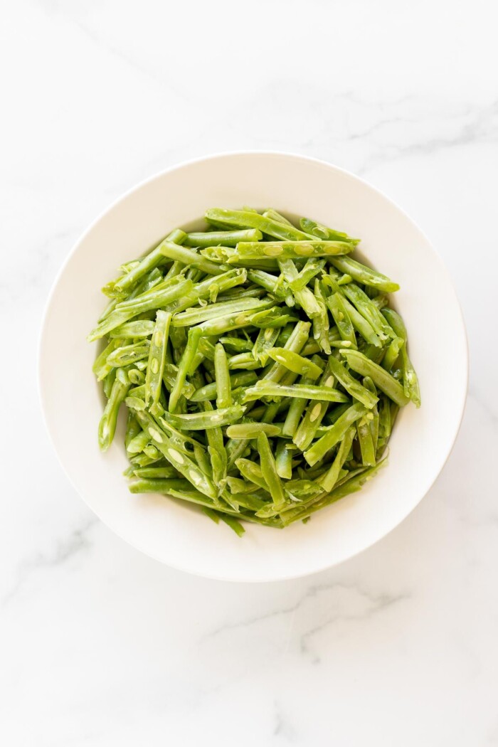 A white bowl on a marble surface, filled with French green beans.