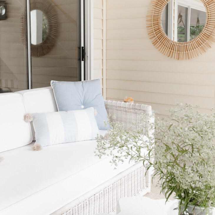 wicker sofa on covered patio with pillows flowers and mirror