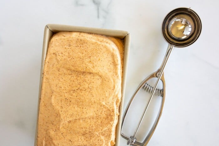 Pumpkin ice cream in a gold loaf pan, on a marble surface.