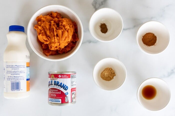 Ingredients for homemade pumpkin ice cream laid out on a marble surface.