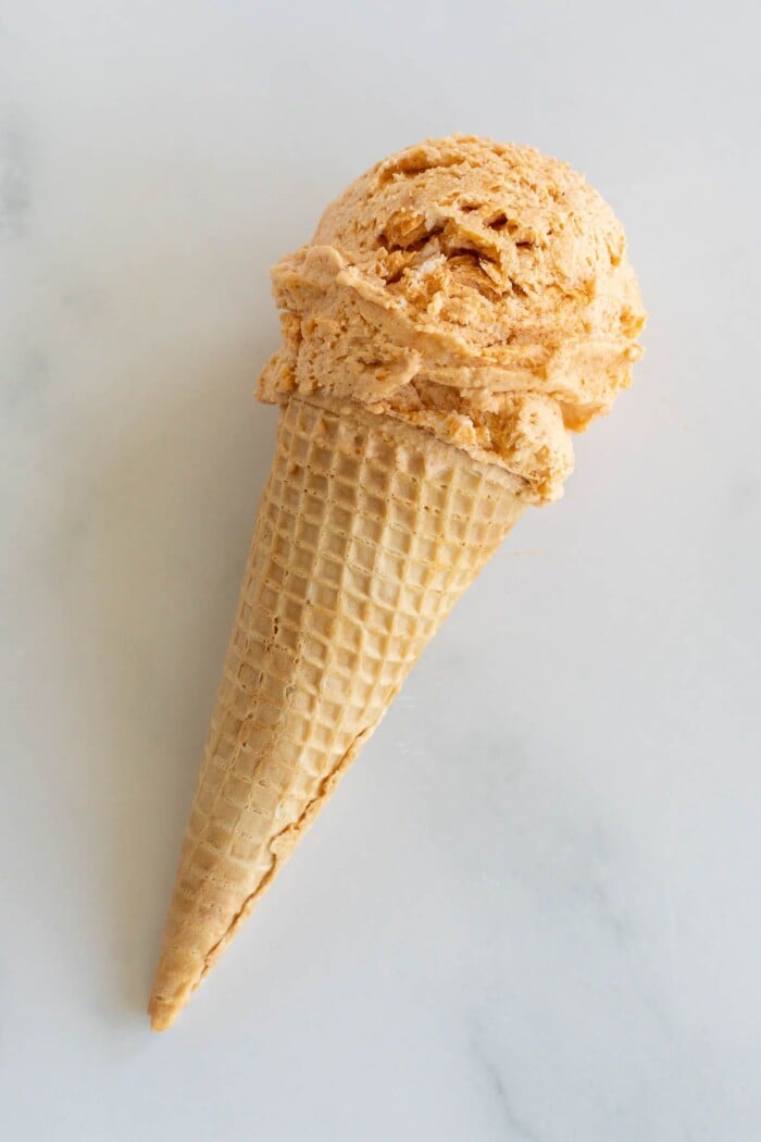 A pumpkin ice cream cone on a marble surface.