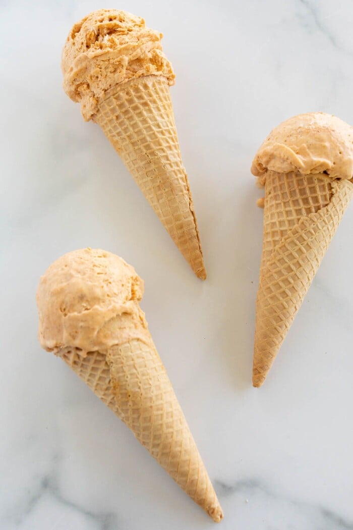 Three ice cream cones full of pumpkin ice cream laying on a marble countertop
