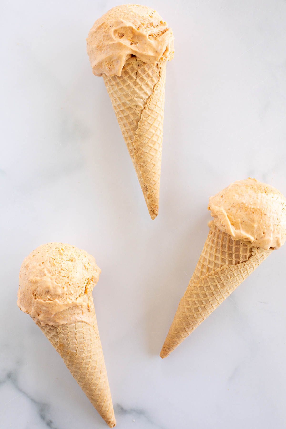 Three ice cream cones full of pumpkin ice cream laying on a marble countertop