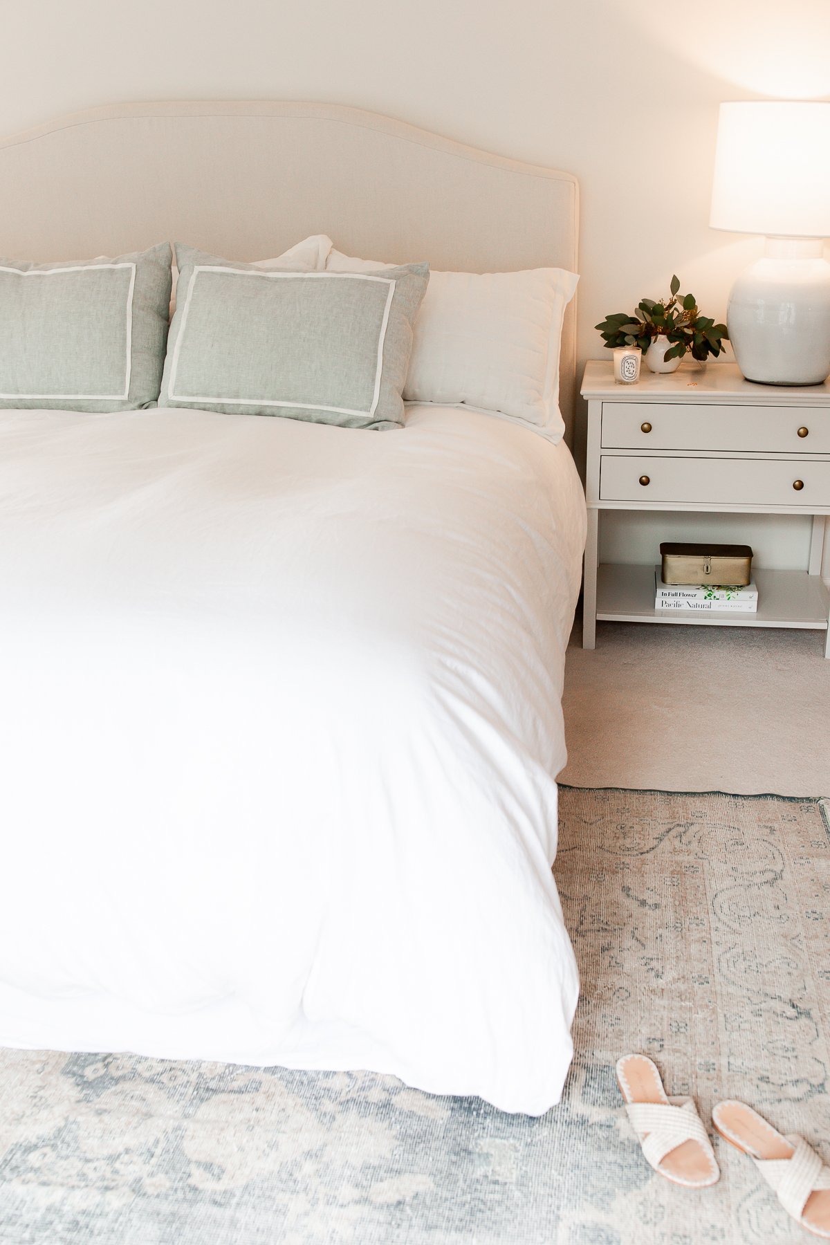 A bed with white bedding and a white nightstand, featuring a rug under the bed