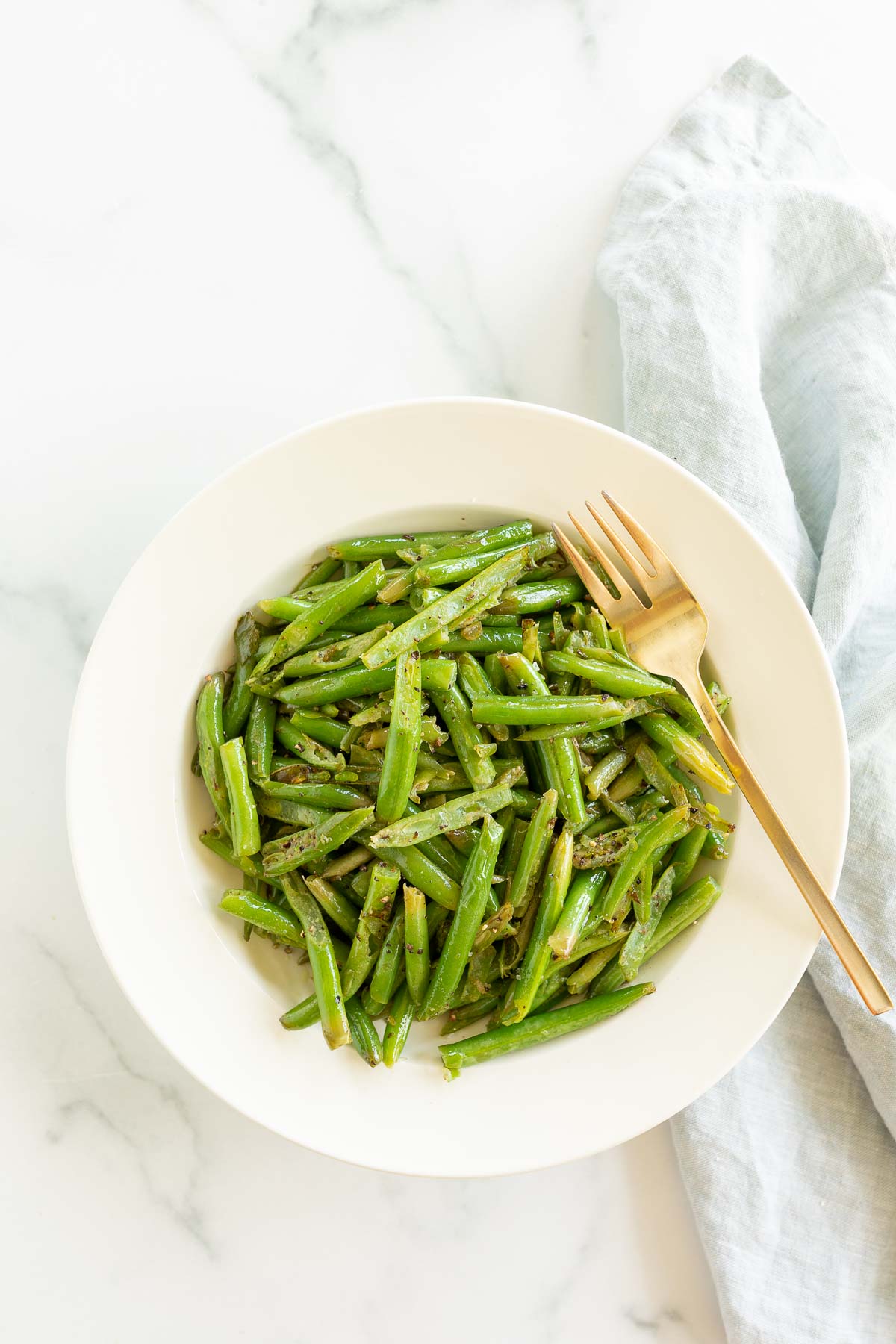 Seasoned green beans in a white bowl with a fork.