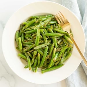 Seasoned green beans served in a white bowl with a gold fork.