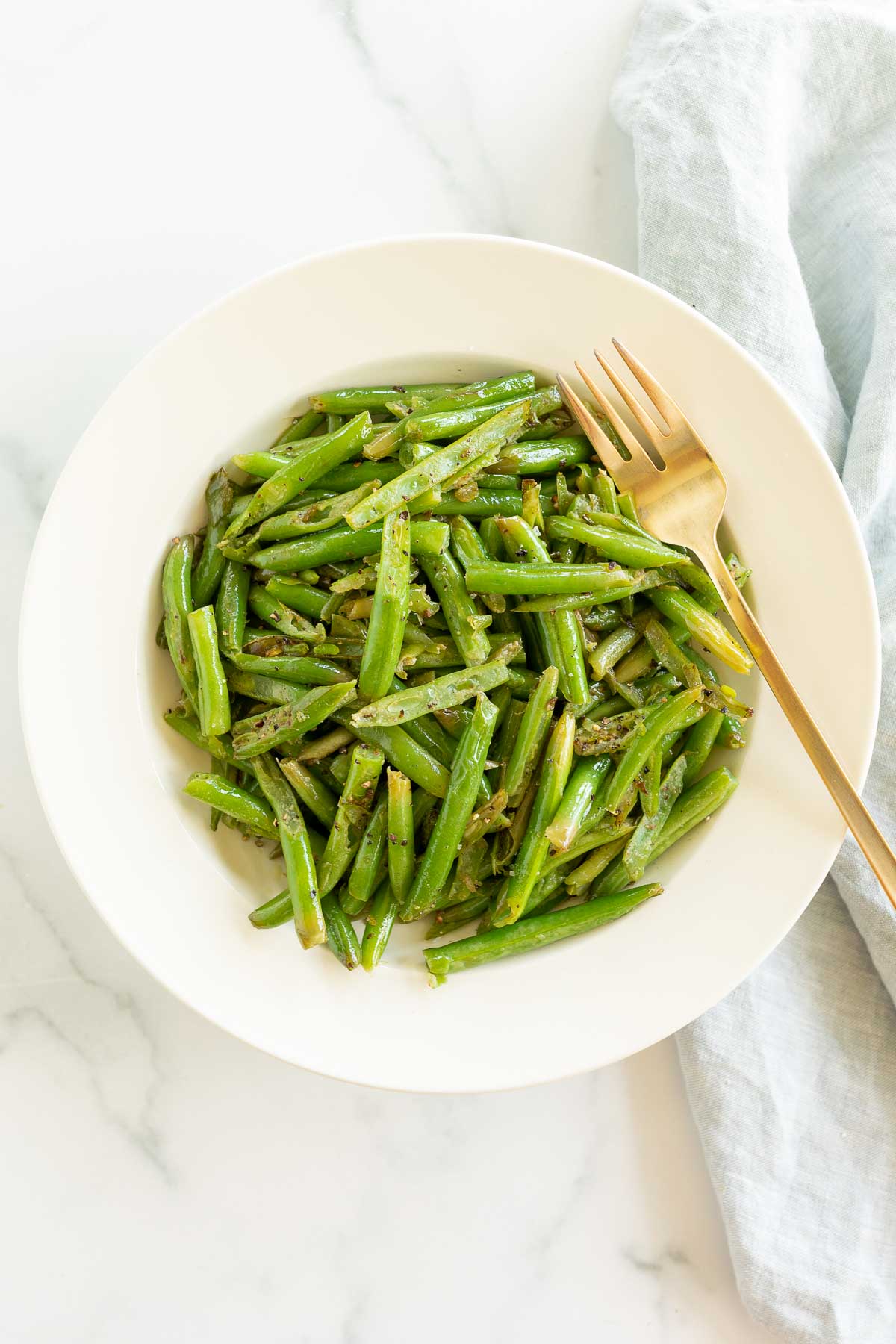 Seasoned green beans served in a white bowl with a gold fork.