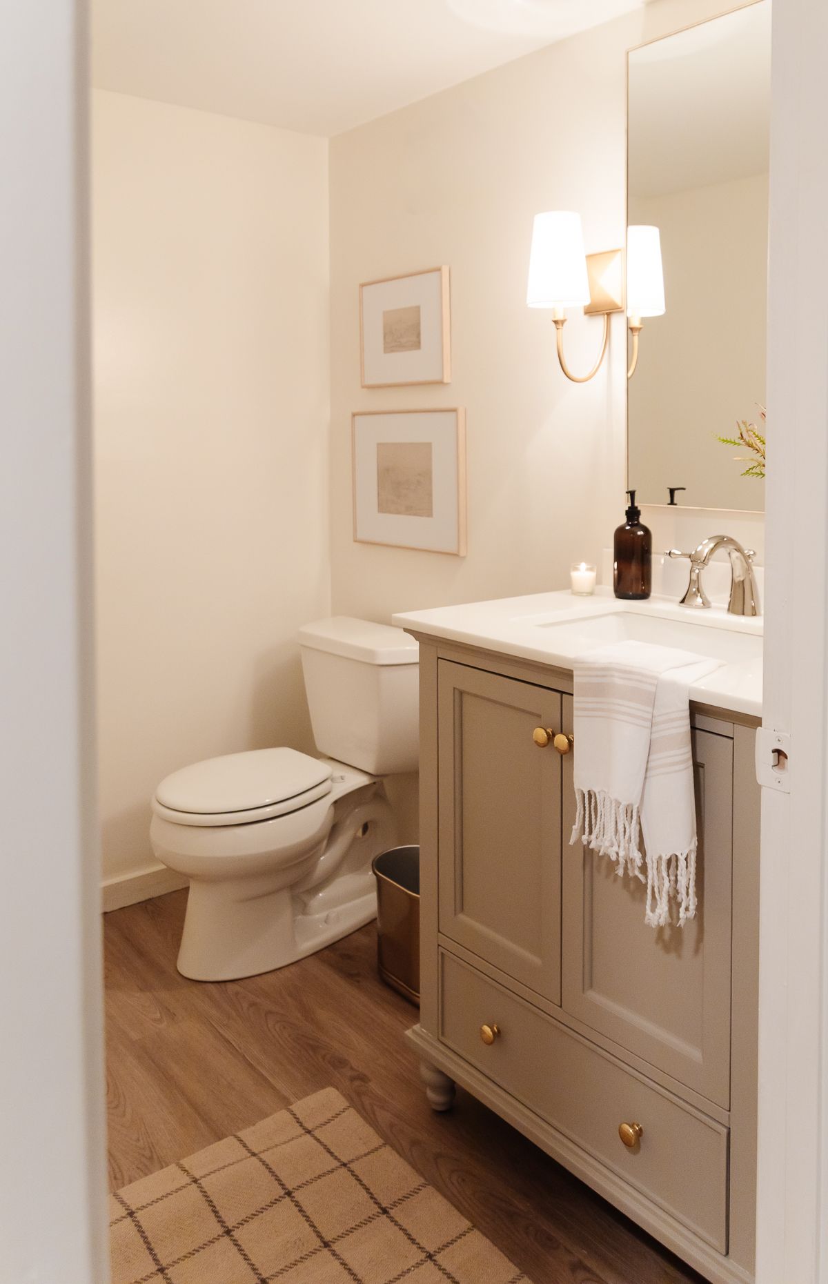 A basement bathroom with a greige painted vanity cabinet and gold sconces