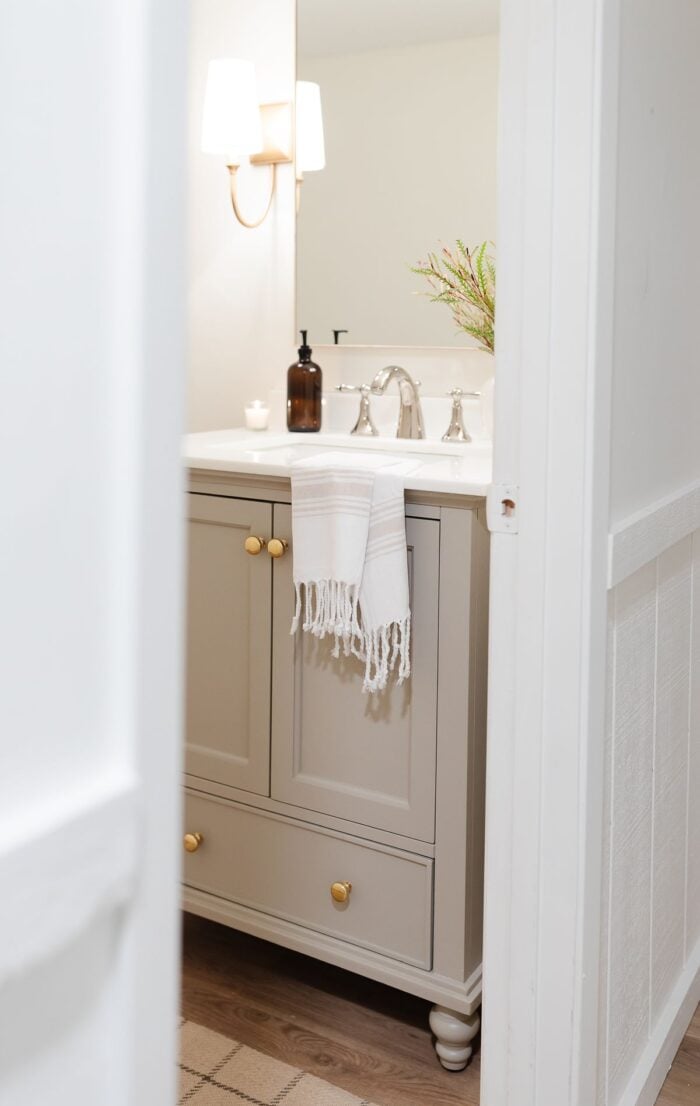 A basement bathroom with a greige painted vanity cabinet and gold sconces