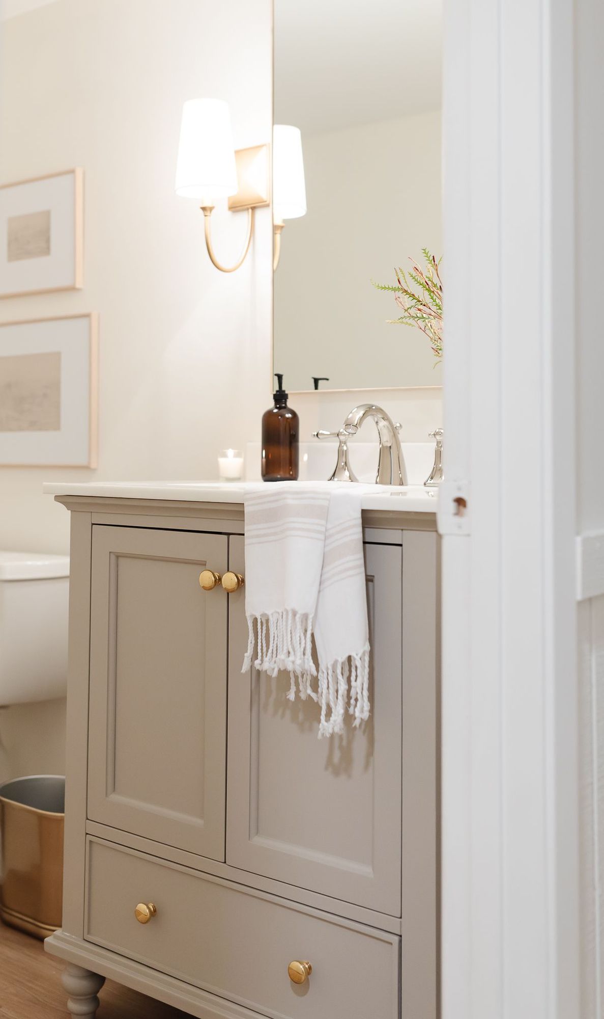 A basement bathroom with a greige painted vanity cabinet and gold sconces