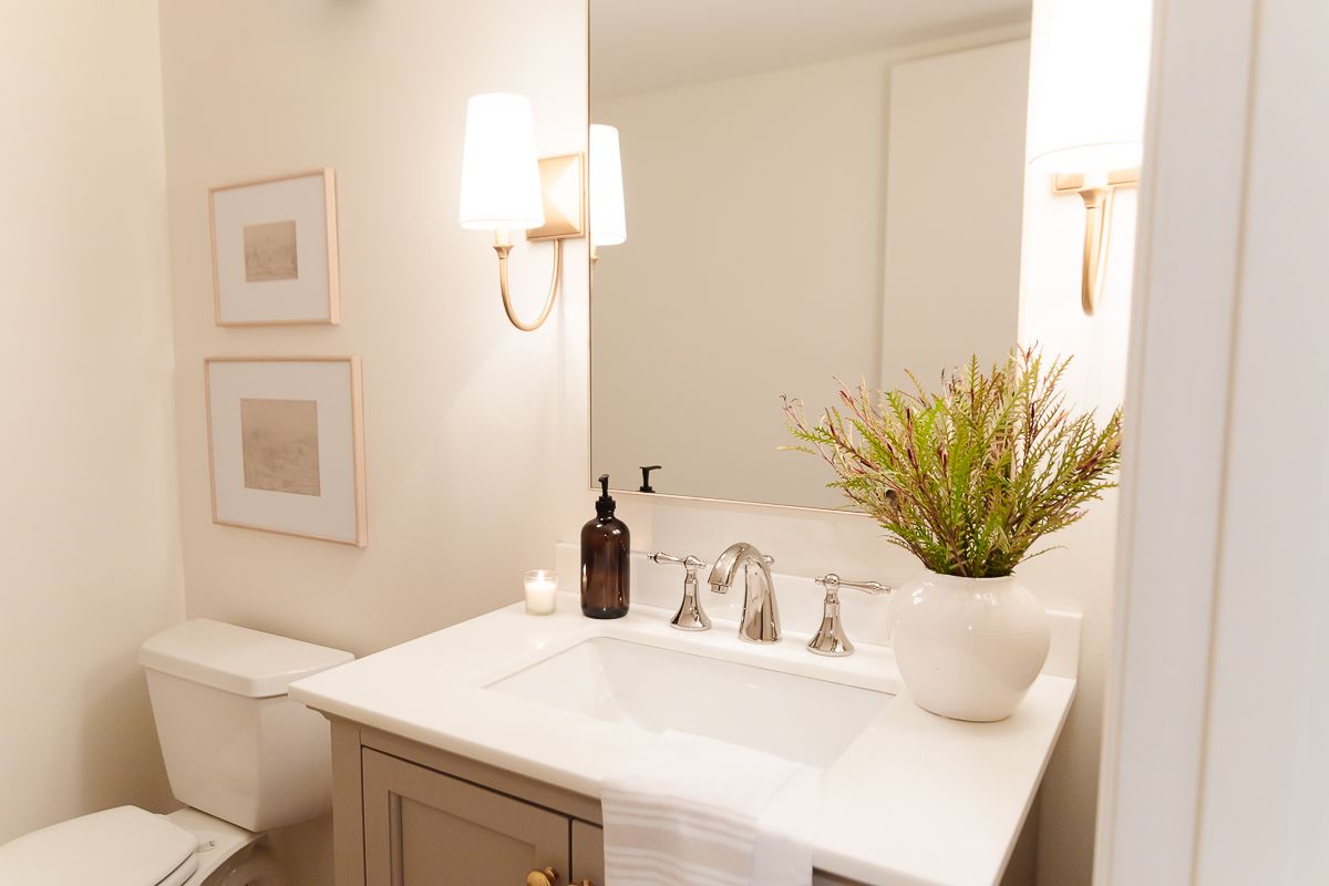 A bathroom in basement with gold sconces and a gray vanity