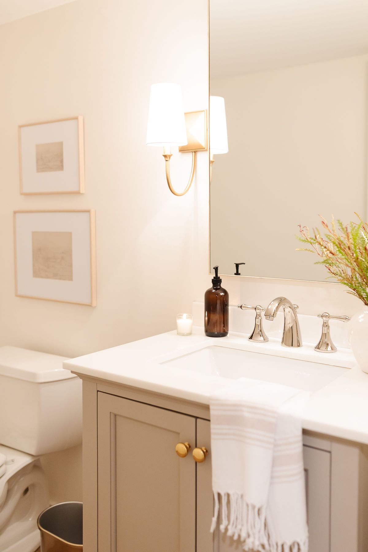 A basement bathroom with a greige painted vanity cabinet and gold sconces