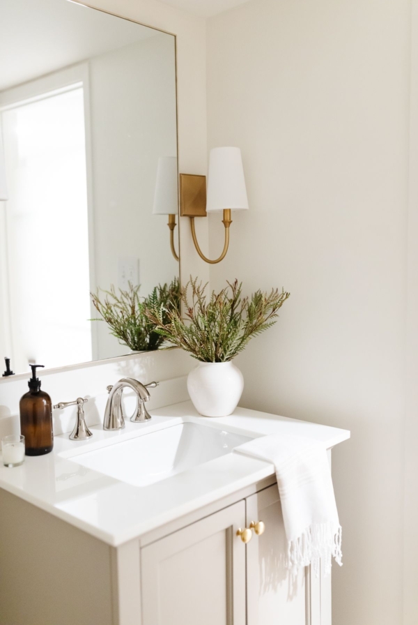 A small bathroom with gold sconces, greige vanity and walls painted Cloud White