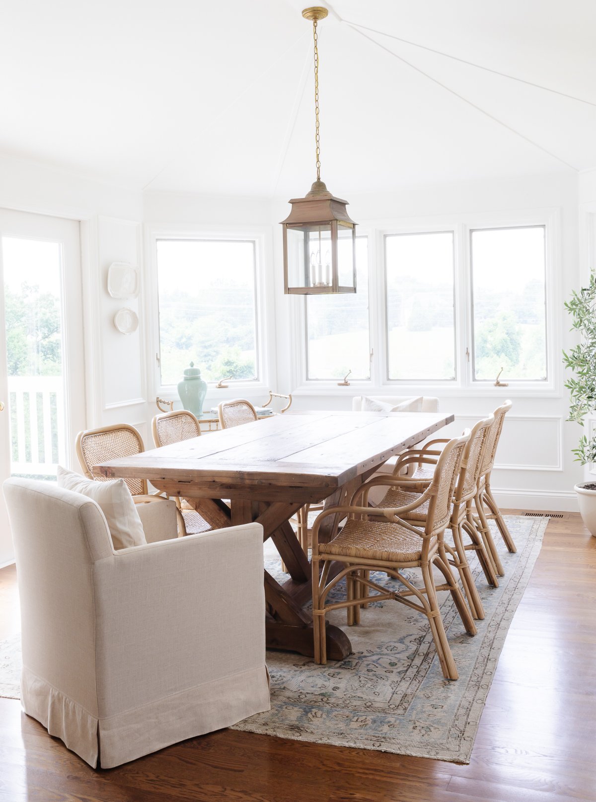 A white dining room with a wood table, rattan chairs and picture frame moulding on the walls.