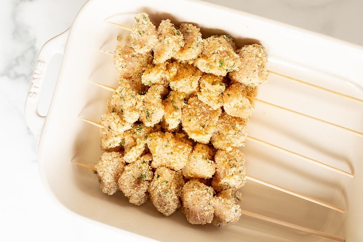 Breaded chicken spiedini skewers before cooking, laid out in a white dish.