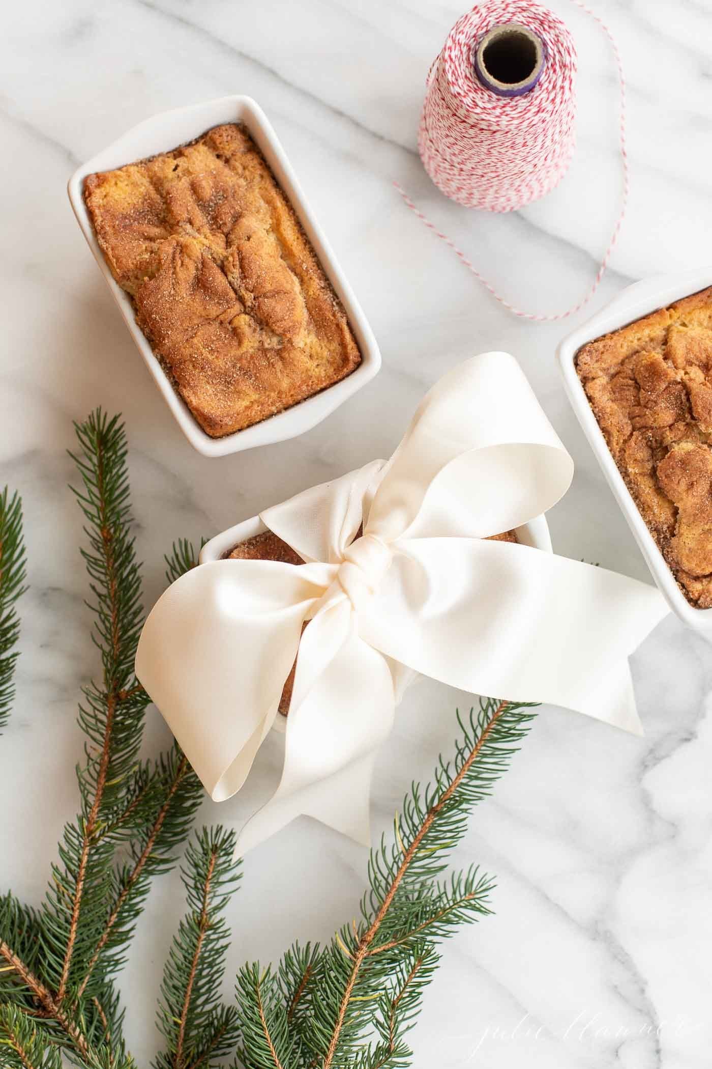 Loaves of cinnamon bread on a marble countertop, with gift wrapping materials nearby, indicating a holiday scene. 