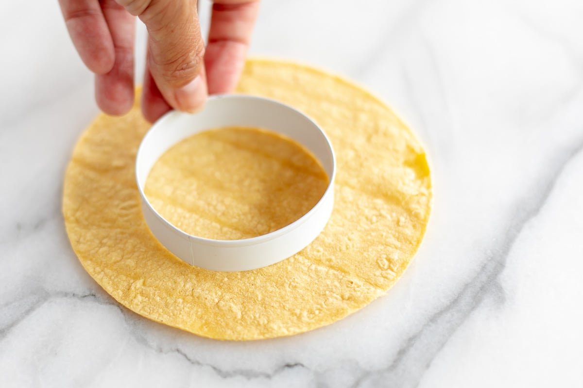 A hand holding a round cookie cutter to make a smaller corn tortilla