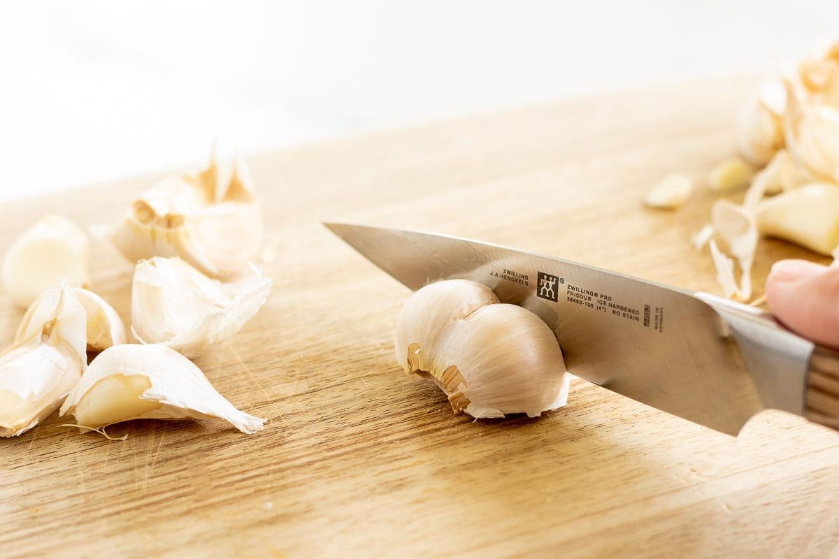 A hand cutting a bulb of garlic on a wooden cutting board