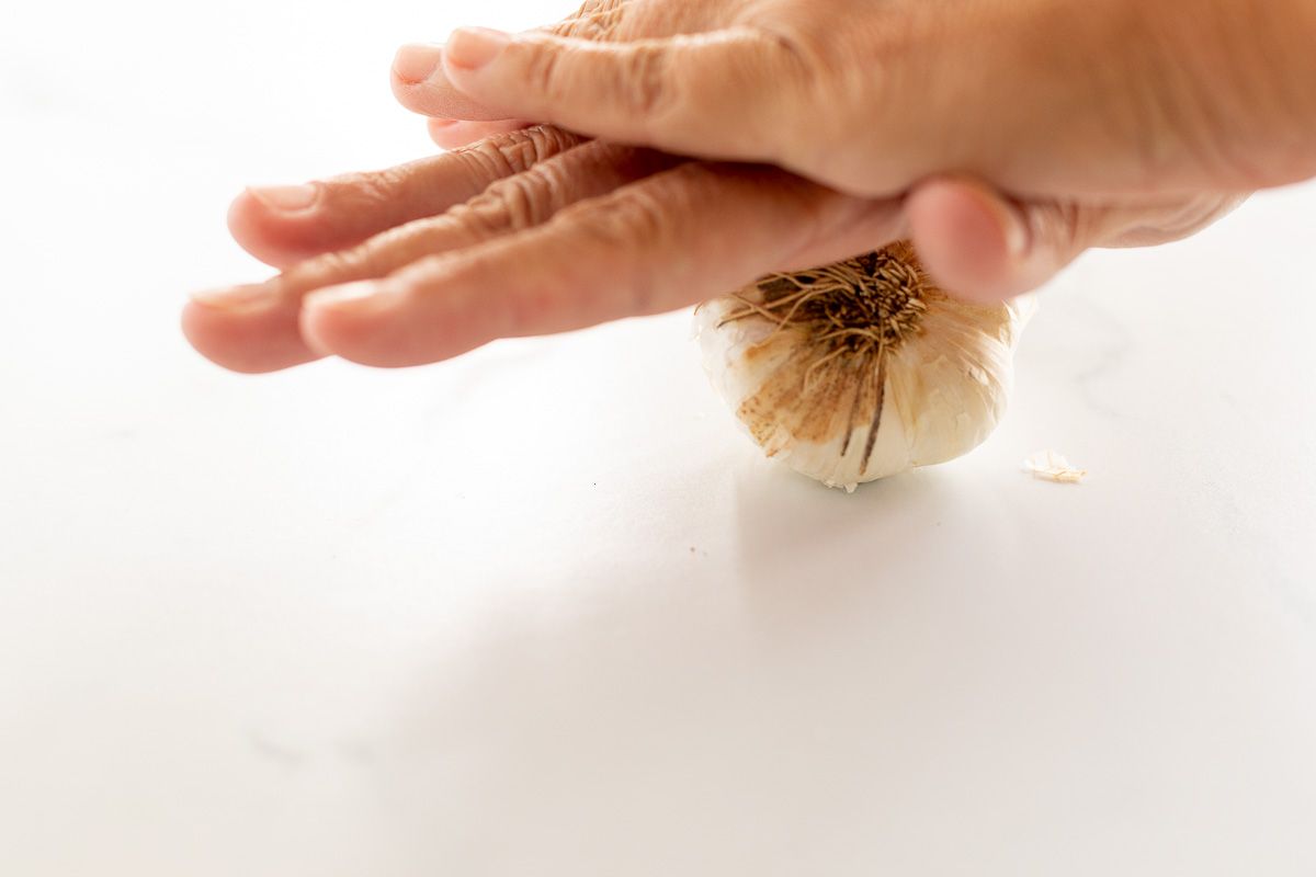 Hands pressing down on a bulb of garlic