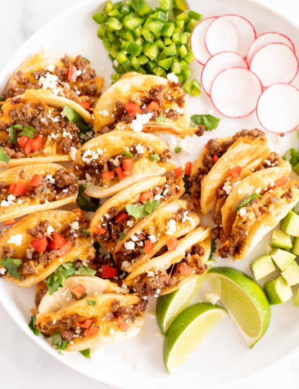 A white platter of mini tacos and toppings.