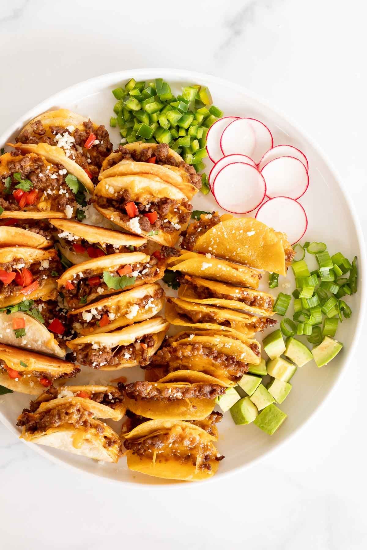 A white platter of mini tacos and toppings.