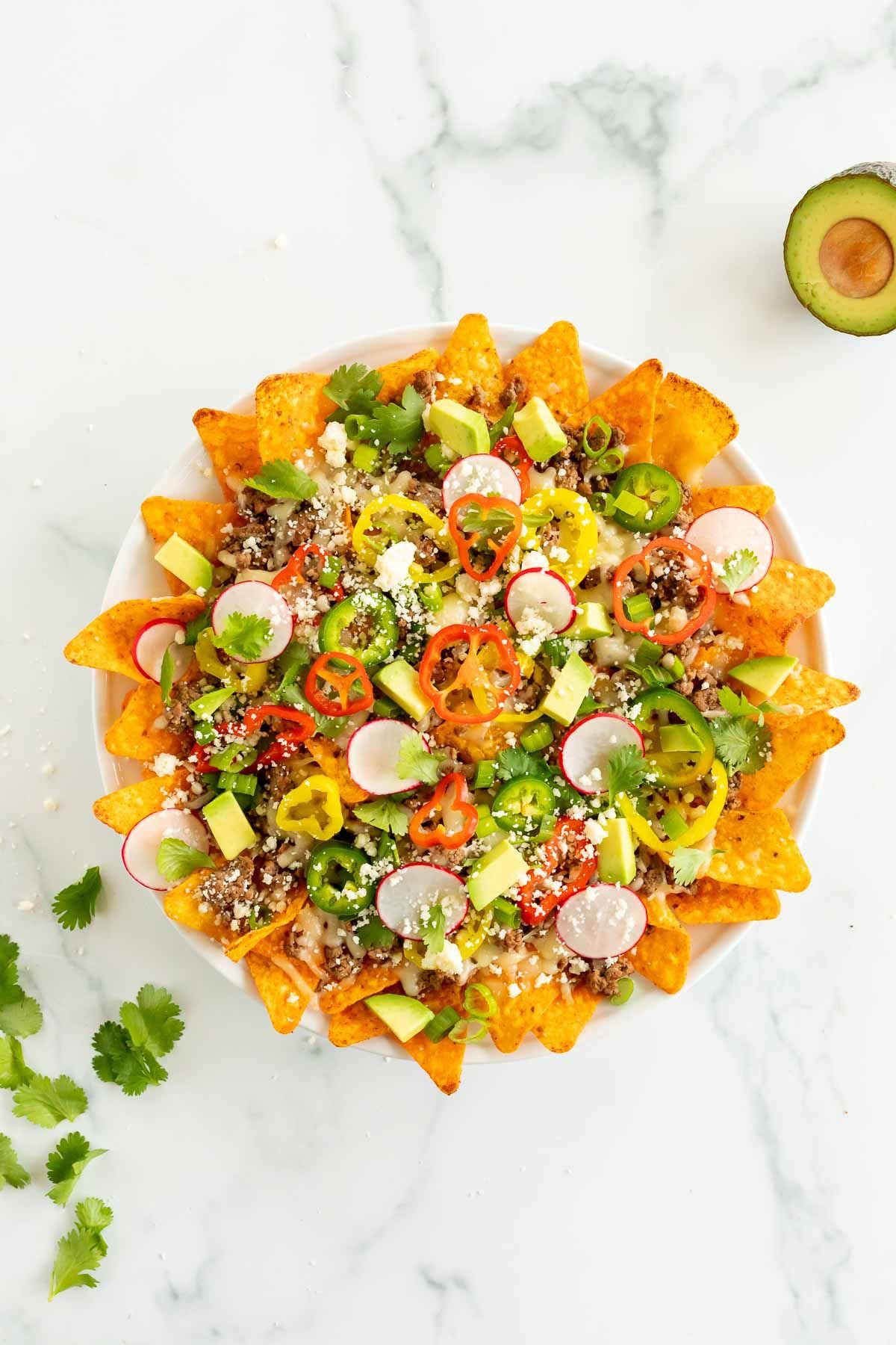 A white plate of nachos with Doritos, loaded with toppings